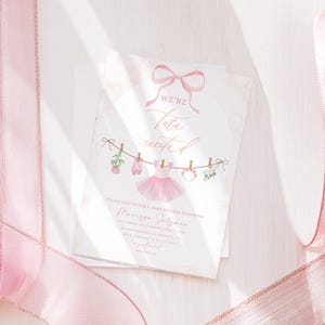 May include: A baby shower invitation with a pink bow and the words "We're Tutu Excited." The invitation features a pink tutu, ballet shoes, and floral accents. The invitation is on a white background with pink ribbon.