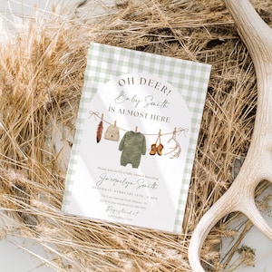 Może przedstawiać: Zaproszenie na baby shower z zielono-białym wzorem w kratkę. Wyświetlany jest tekst "OH DEER! Baby Smith IS ALMOST HERE". Zawiera ilustracje ubranek dla dzieci i poroża. Zaproszenie otoczone jest suchą trawą i porożem jelenia.