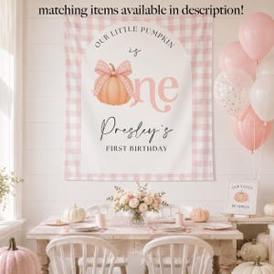Op de afbeelding: Een rechthoekige stoffen achtergrond met een roze en witte gingham rand, een centrale boog en een perzikkleurige pompoen met een roze geruite strik. De tekst luidt: Our Little Pumpkin is one, Presley's First Birthday. Bijpassende items beschikbaar.