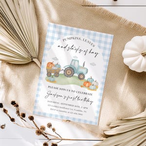 Może przedstawiać: Jasnoniebieskie zaproszenie w kratkę z napisem "Pumpkins, Leaves and stacks of hay". Zaproszenie zawiera akwarelową ilustrację traktora ciągnącego wózek wypełniony dyniami. Tekst brzmi "Jackson's first birthday."