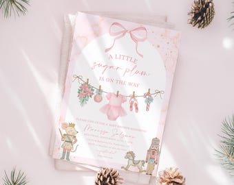 May include: A baby shower invitation with a pink and gold marble design. The invitation features the text "A little sugar plum is on the way" and illustrations of baby clothes and ballet shoes. The invitation is decorated with pinecones and greenery.