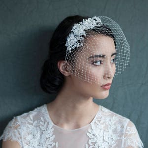 Puede incluir: Una novia con un vestido blanco de encaje con un delicado patr&oacute;n floral y un velo blanco con un adorno de cuentas.