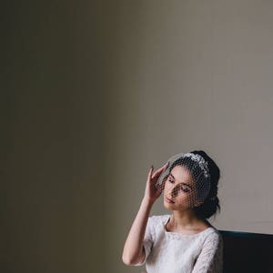 Puede incluir: Una mujer con un vestido blanco de encaje y un velo, sentada en una silla con la mano en la cabeza.