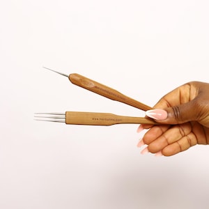 May include: Two bamboo dreadlock tools with metal tips. One tool has a single needle, the other has three. The text "@dreadsbyfms 0.5mm" and "www.hairbyfms.com" are printed on the tools. The tools are held against a white background.