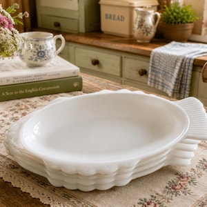Peut inclure: Une pile de quatre assiettes en verre opalin blanc en forme de poisson, présentant une surface intérieure lisse et un design texturé au niveau de la queue et des nageoires sur les bords. Les assiettes sont ovales avec une finition brillante.