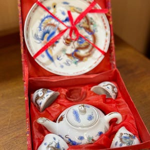 Op de afbeelding: Een wit porseleinen theeservies met een drakenontwerp in een rode doos. De set bevat een theepot, vier kopjes en een klein bord. De doos is gevoerd met rood satijn.