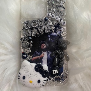 May include: A clear phone case with a black and white glitter design. The case features a photo of Rod Wave, a Hello Kitty character, a crown, a black teddy bear, and the word "LOVE" in white beads. The case also has a black "M" charm.