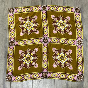 May include: Square brown scarf with a repeating floral pattern in yellow, pink, and white. The scarf has a border of pink and yellow floral designs. The word "Echo" is printed in the bottom right corner.