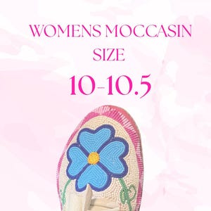 May include: A close-up of a cream-colored moccasin with a beaded blue flower design. The shoe is size 10-10.5. The text "WOMENS MOCCASIN SIZE" is displayed above the shoe in pink.