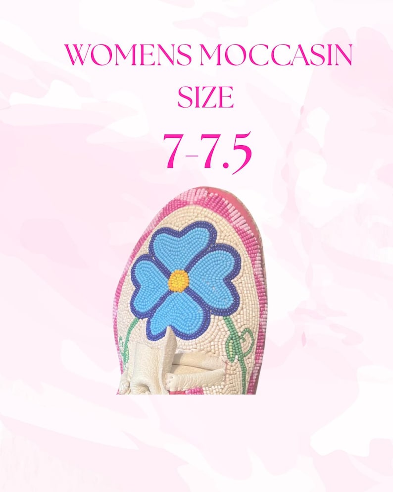 May include: A close-up of a cream-colored moccasin with a beaded blue flower design. The moccasin has a pink and white beaded border. The text "WOMENS MOCCASIN SIZE 7-7.5" is displayed in pink.