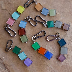 May include: A collection of six keychains, each featuring a silver-toned metal carabiner clip attached to a short chain of three square, translucent glass tiles in various colors including lime green, blue, pink, orange, and purple.