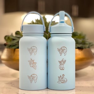 Puede incluir: Dos botellas de agua azul claro con tapa blanca y asa de transporte. Las botellas tienen un gráfico de una criatura de dibujos animados.
