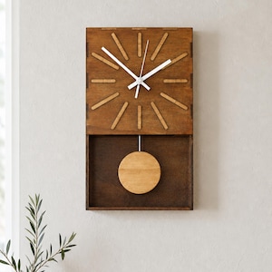 Peut inclure: Une horloge murale rectangulaire en bois avec une finition brun foncé. Le cadran présente douze marqueurs en bois brun clair et des aiguilles blanches. Sous le cadran, un pendule circulaire en bois brun clair est suspendu dans un cadre ouvert.