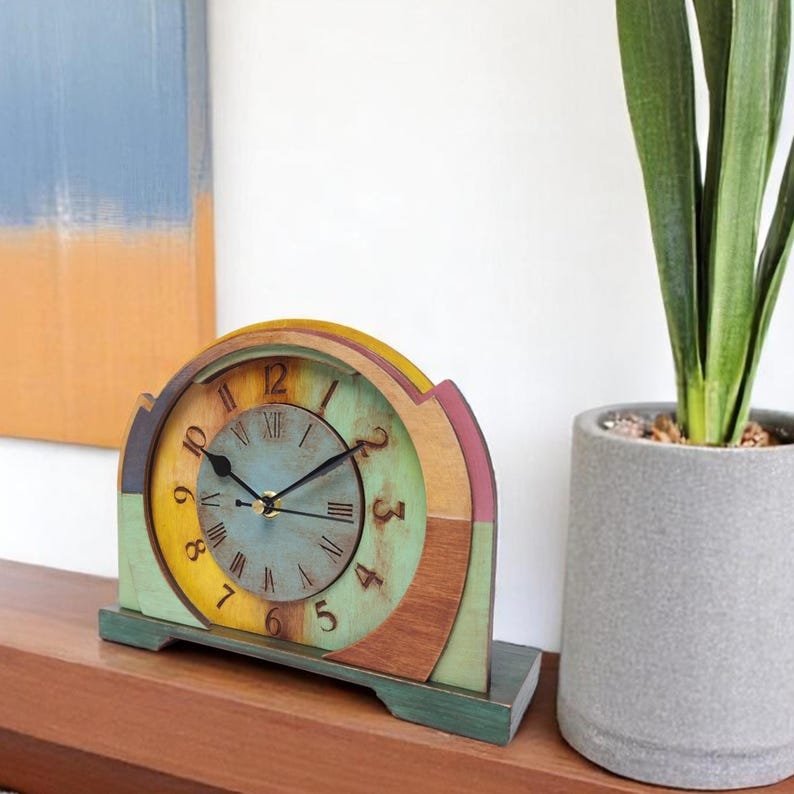 May include: A multi-coloured wooden mantel clock with a round face and Roman numerals. The clock has a design with yellow, green, and brown hues. The clock is set on a wooden surface.