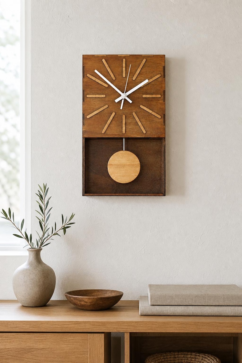 Puede incluir: Un reloj de pared rectangular de madera marr&oacute;n oscuro con una esfera estilo rayos de sol que presenta marcadores de hora de madera clara. Tiene manecillas blancas y un p&eacute;ndulo circular de madera clara que oscila en un compartimento abierto.