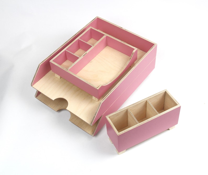 Op de afbeelding: Een set roze houten bureau-organizers met natuurlijke houten interieurs. De set bevat een grote lade, een kleinere lade met vakken en een rechthoekige doos met drie secties. Voor op kantoor of thuis.