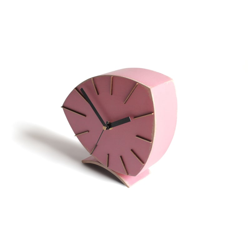 Peut inclure: Une horloge en bois rose avec des aiguilles noires et des accents dor&eacute;s. L'horloge est en forme d'&eacute;ventail et a une base incurv&eacute;e.