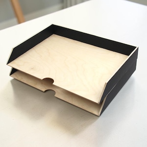 May include: A two-tiered wooden desk organizer with a natural wood interior and black painted exterior. The organizer has a cutout on the front for easy access to the contents. The desk organizer is designed to hold papers and other office supplies.