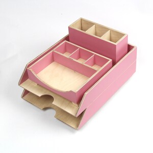 Op de afbeelding: Een roze houten bureau-organizer met meerdere compartimenten en laden. De organizer bevat een pennenhouder, een lade met verdelers en een papieren lade met twee niveaus. De binnenkant van de compartimenten is van natuurlijk hout.