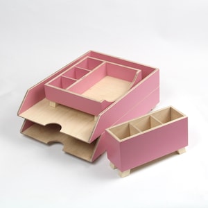 Op de afbeelding: Een set roze houten bureau-organizers. De set bevat een gelaagde brievenbak, een kleine organizer met compartimenten en een rechthoekige pennenhouder met drie secties. De interieurs zijn van natuurlijk hout.