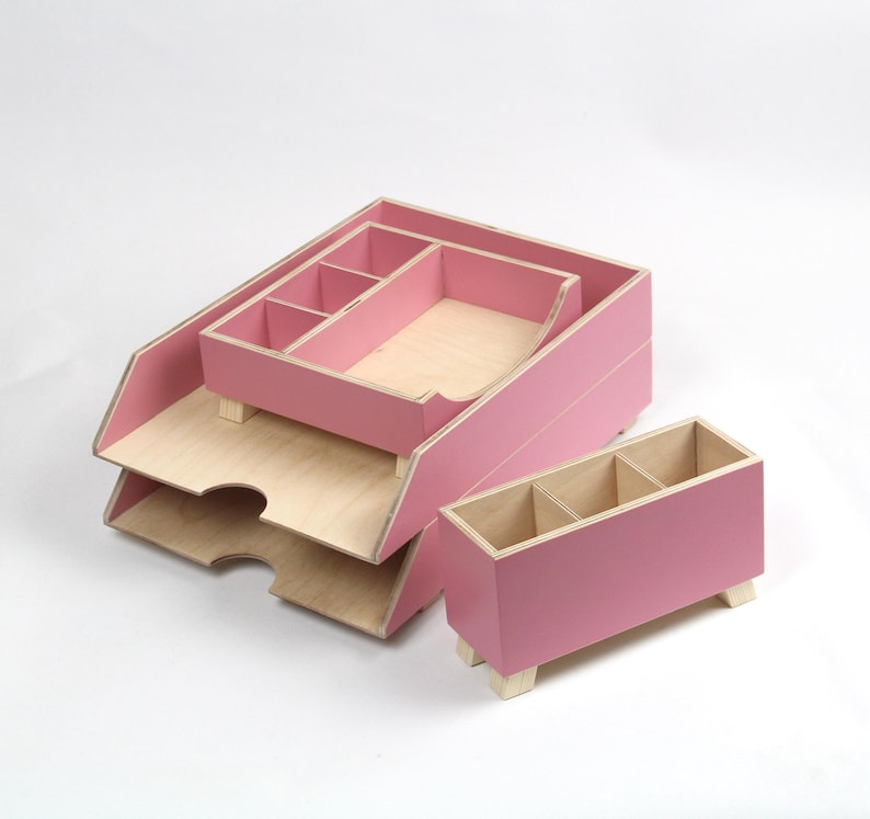 Op de afbeelding: Een set roze houten bureau-organizers. De set bevat een gelaagde brievenbak, een kleine organizer met compartimenten en een rechthoekige pennenhouder met drie secties. De interieurs zijn van natuurlijk hout.