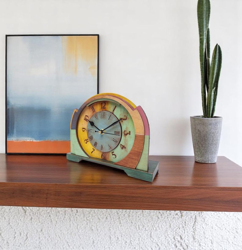 May include: A colourful wooden mantel clock with a vintage design. The clock face is light blue with black hands and Roman numerals. The clock's frame features a rainbow of colours, including yellow, green, and pink. The clock is approximately 25 cm wide.