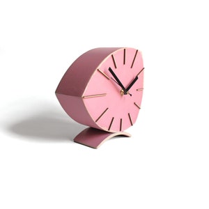 Peut inclure: Une horloge en bois rose avec une base incurv&eacute;e et des marqueurs d'heures dor&eacute;s. Le cadran de l'horloge est en forme de larme.