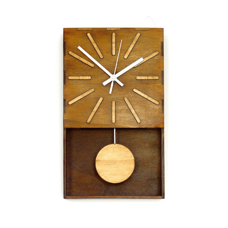 Puede incluir: Un reloj de pared rectangular hecho de madera marr&oacute;n oscura con un acabado de madera m&aacute;s clara en el p&eacute;ndulo circular y los marcadores de hora. La esfera tiene manecillas blancas y doce marcadores rectangulares espaciados.