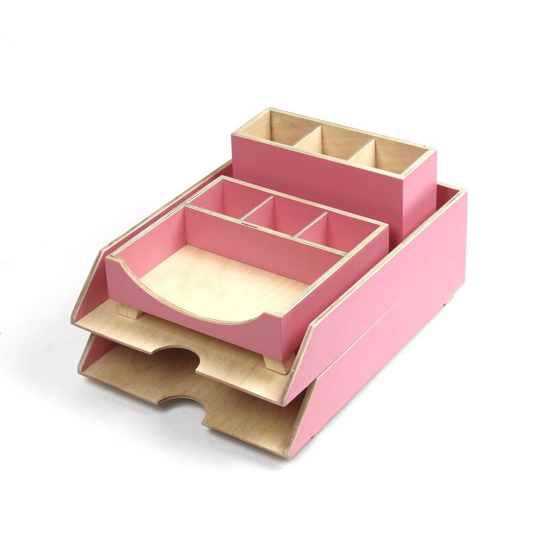 Op de afbeelding: Een roze houten bureau-organizer met meerdere compartimenten en trays. De organizer heeft een licht houten interieur en een roze buitenkant. Het bevat een pennenhouder, een tray met verdelers en een papierlade met twee niveaus.