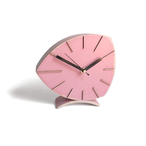 Peut inclure: Une horloge en bois rose avec un design unique en forme de feuille. L'horloge a des aiguilles noires et des accents dor&eacute;s.