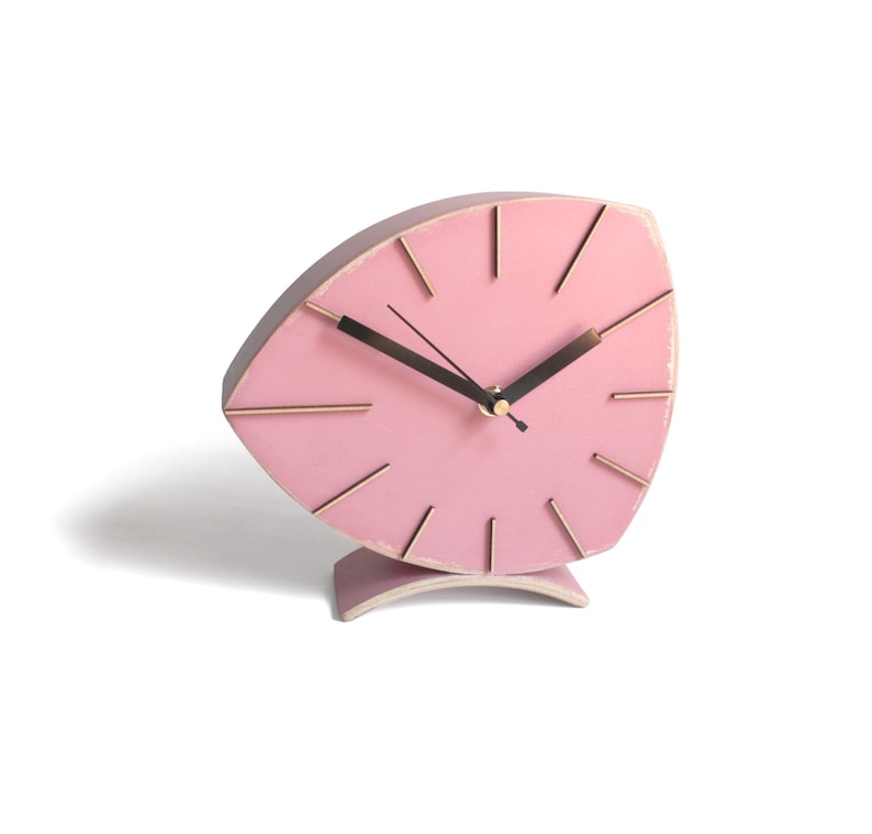 Peut inclure: Une horloge en bois rose avec un design unique en forme de feuille. L'horloge a des aiguilles noires et des accents dor&eacute;s.