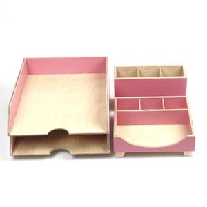 Op de afbeelding: Een tweedelige bureau-organizer set. De set bevat een papierbak met twee niveaus en een bureau-organizer met meerdere compartimenten. Beide stukken zijn gemaakt van lichtgekleurd hout met roze accenten op de randen en verdelers.