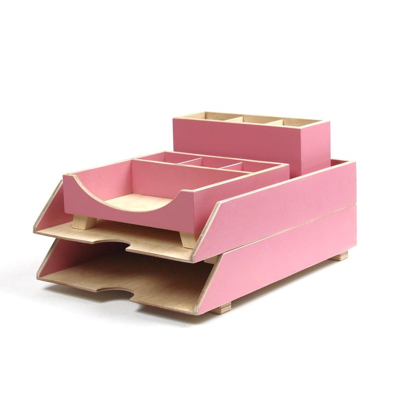 Op de afbeelding: Een roze houten bureau-organizer met meerdere compartimenten en trays. De organizer heeft een gelaagd ontwerp, met een pennenhouder, een tray met verdelers en twee papiertrays. Het hout heeft een natuurlijke afwerking aan de binnenkant en een roze buitenkant.