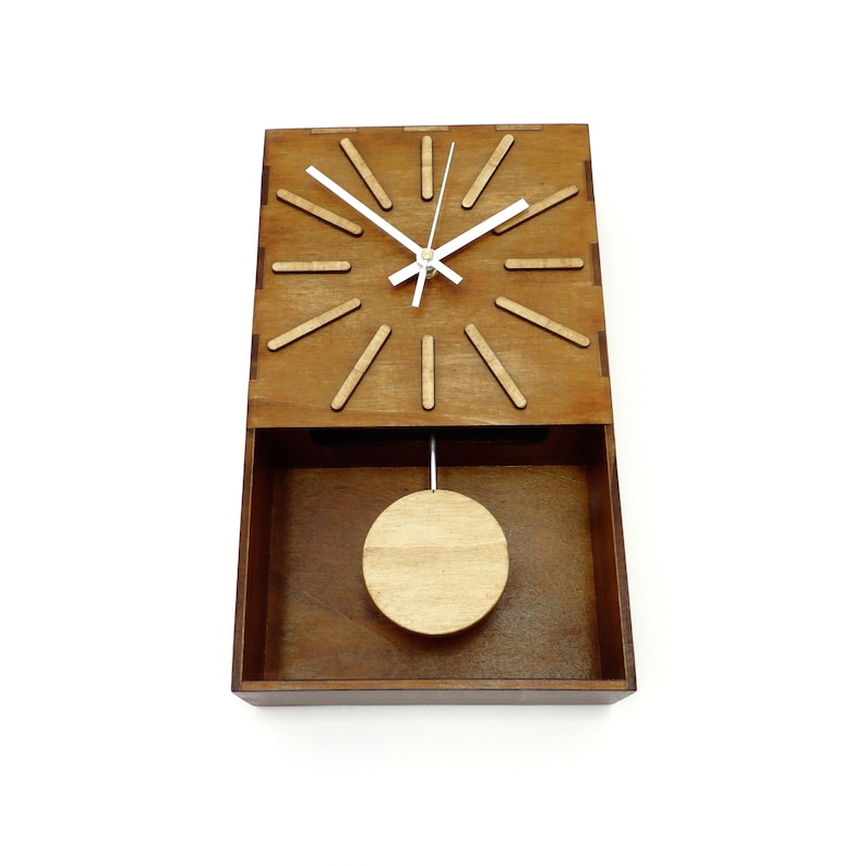 Puede incluir: Un reloj de pared rectangular de madera con acabado marr&oacute;n oscuro. La esfera presenta doce marcadores de hora de madera clara, manecillas blancas y un p&eacute;ndulo circular suspendido en la secci&oacute;n inferior abierta del marco de madera.