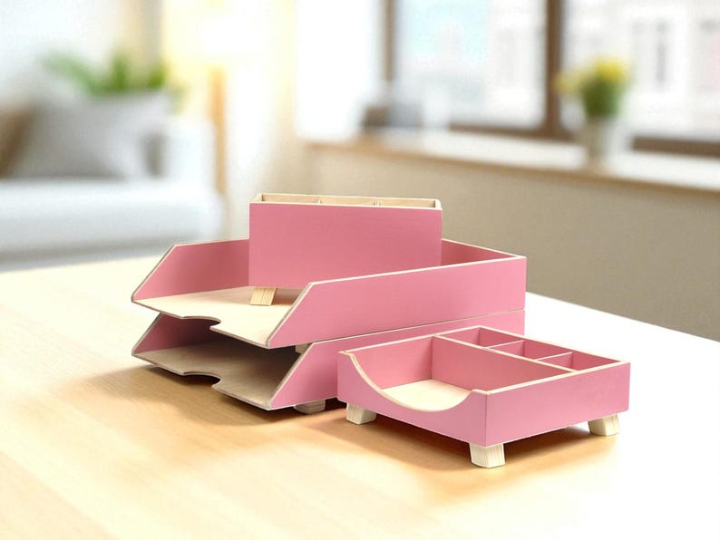 Op de afbeelding: Een set roze houten bureau-organizers. De set bevat een papierbak met twee niveaus, een pennenhouder en een klein dienblad met vakken. De organizers hebben een licht houten interieur.