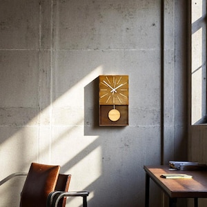 Puede incluir: Un reloj de pared rectangular de madera con esfera marr&oacute;n claro, marcadores de hora blancos y manecillas blancas. Debajo de la esfera, un p&eacute;ndulo circular de madera cuelga dentro de un marco abierto, suspendido por una varilla met&aacute;lica fina.