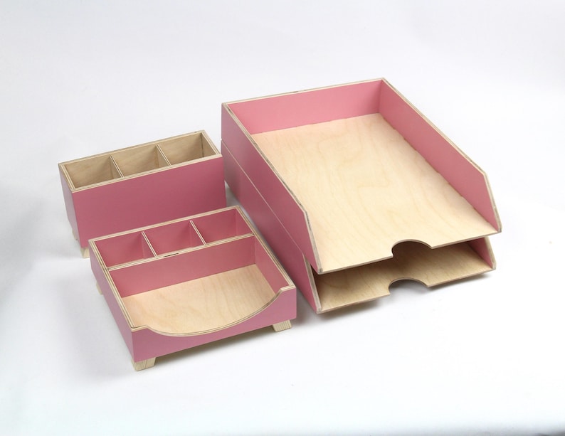 Op de afbeelding: Een set van drie houten bureau-organizers in lichtroze. De set bevat een rechthoekige pennenhouder met drie compartimenten, een vierkante organizer met vier compartimenten en een lade met twee niveaus. De interieurs zijn van natuurlijk hout.