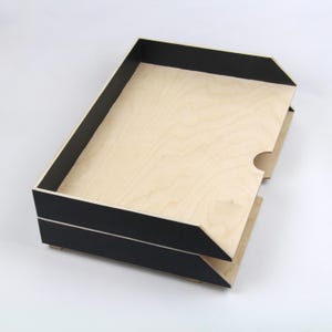 Może przedstawiać: Drewniany organizer na dokumenty z dwoma poziomami. Organizer jest wykonany z naturalnego drewna z czarnymi krawędziami.