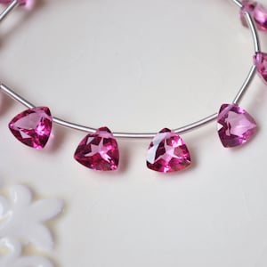 May include: A strand of pink gemstone beads, each bead is a triangular faceted shape, strung on a silver wire.