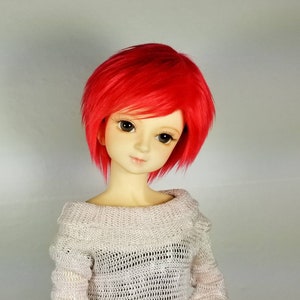 May include: A doll with short, bright red hair wearing a white knitted sweater.