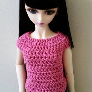 May include: A doll wearing a pink crocheted top with short sleeves and blue jeans.