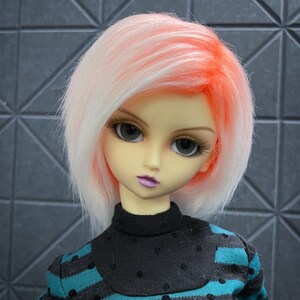 May include: A doll with a pale complexion, large gray eyes, and a short, layered hairstyle. The hair is white with orange and pink highlights. The doll wears a black turtleneck sweater with teal and black striped sleeves.