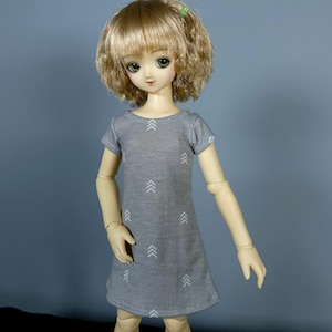May include: A gray doll dress with white arrow patterns. The dress has short sleeves and a round neckline.