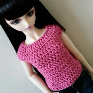 May include: A pink crocheted top with short sleeves and a scoop neck. The top is made with a textured stitch and is perfect for a doll.