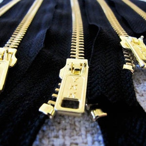 Puede incluir: Varias cremalleras de color dorado con cinta negra. Las cremalleras tienen el nombre de la marca YKK en el deslizador.