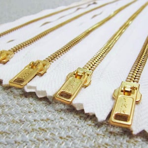 May include: Four gold metal zippers with white tape. The zippers have a YKK logo on the pull tabs.