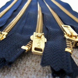 May include: Multiple gold-coloured zippers with navy blue tape. The zippers are laid out in a row, with the pull tabs facing the viewer.