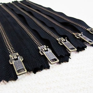 Könnte beinhalten: Ein Satz mit sechs schwarzen Reißverschluss-Zügen mit Messing-Schiebern. Jeder Schieber hat den Text "YKK" aufgedruckt.