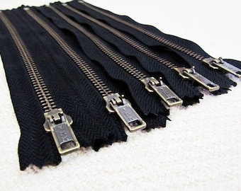 May include: A set of six black zipper pulls with brass sliders. Each slider has the text "YKK" printed on it.