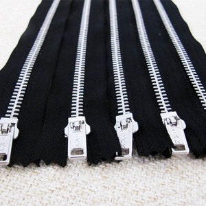 May include: Six silver metal zippers with black tape. The zippers are all closed and have a silver slider.